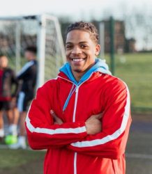 A portrait of a young mixed race man looking into the camera with his team mates in the background.